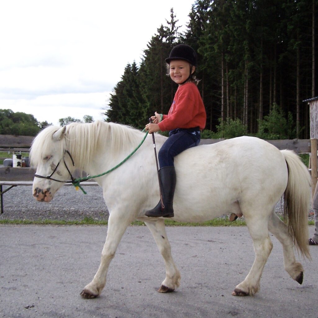 Dana Künstner als Kind beim Reiten ohne Sattel auf einem weißen Pony mit Halfter